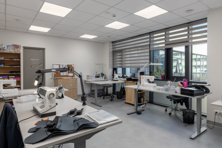 Moderns, labi apgaismots birojs ar vairākiem rakstāmgaldiem, krēsliem, datoriem, šujmašīnām, piederumiem un lieliem logiem ar žalūzijām. Pie aizmugurējās sienas ir plaukti ar grāmatām un kastēm. Telpa ir sakopta un organizēta.