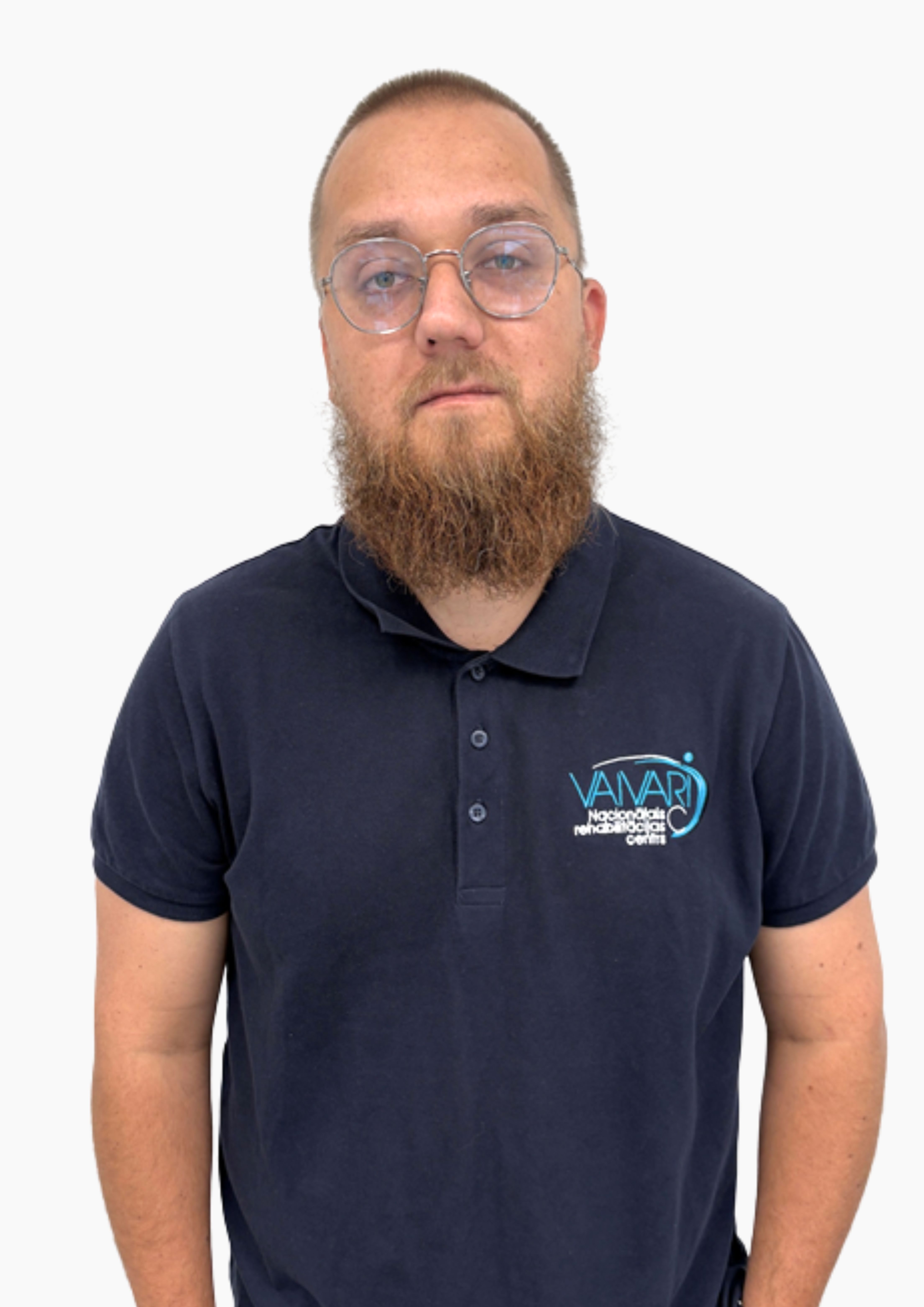 Vīrietis ar bārdu un brillēm, kurš valkā tumši zilu polo kreklu ar Vanari Neirozinātņu centra logotipu, stāv uz vienkārša balta fona.