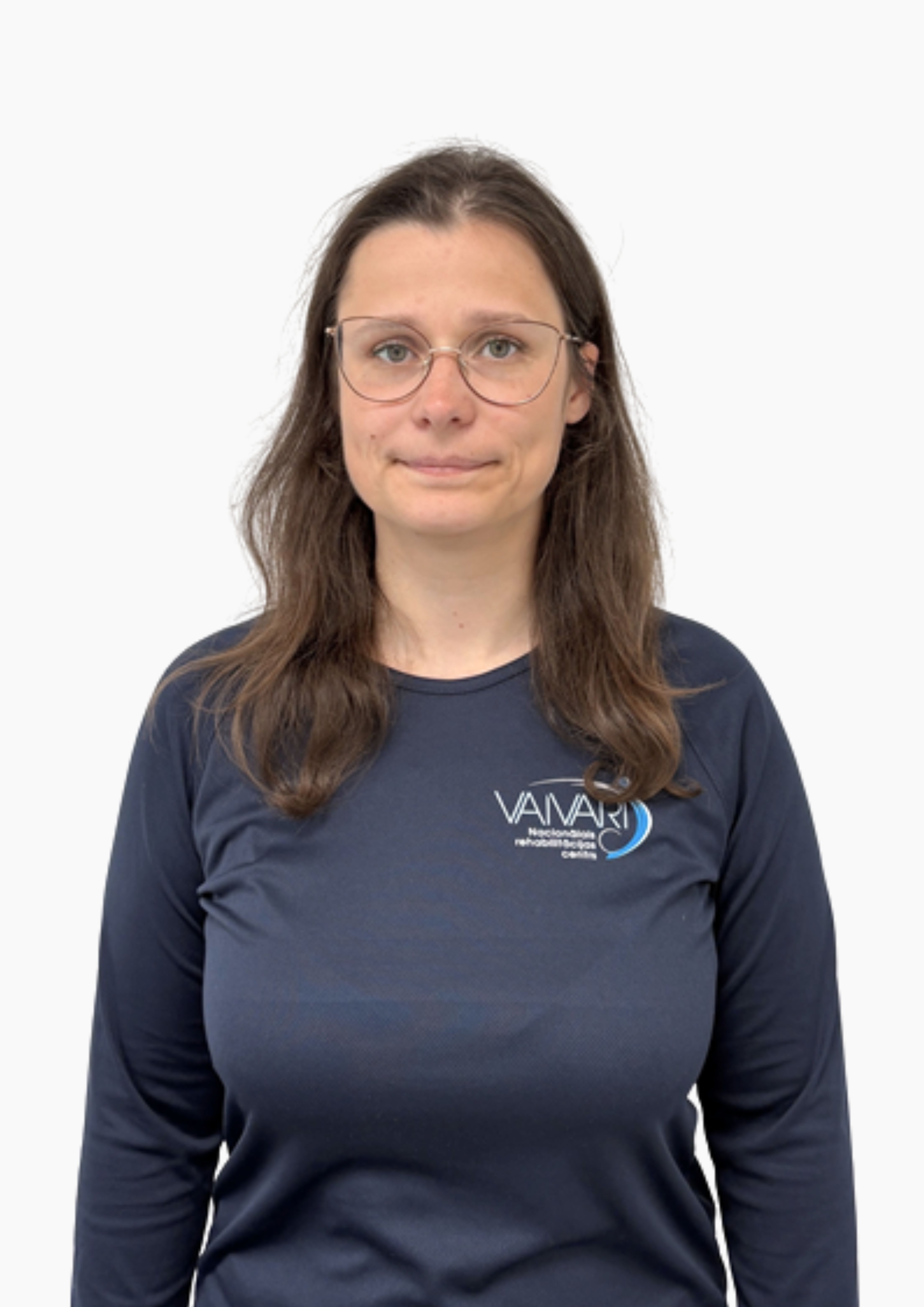 Sieviete ar gariem brūniem matiem, brilles un tumši zilu kreklu ar uzrakstu „VAIARI“ stāv uz vienkārša balta fona un ar neitrālu sejas izteiksmi skatās tieši kamerā.
