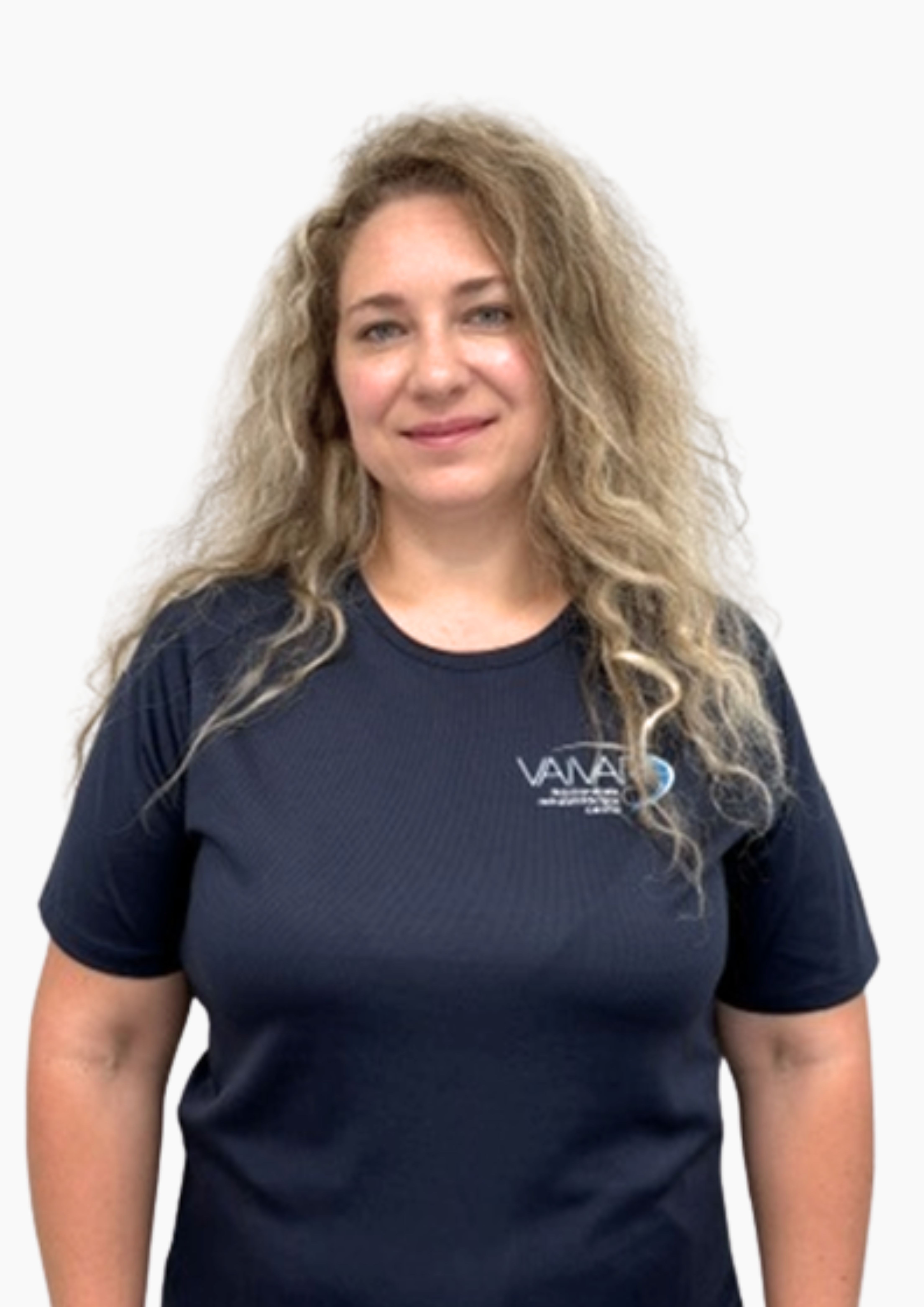 Sieviete ar gariem, cirtainiem blondiem matiem smaida un ir tērpusies tumši zilā T-kreklā ar nelielu „VANA“ logotipu kreisajā krūšu pusē; viņa stāv uz vienkārša balta fona.